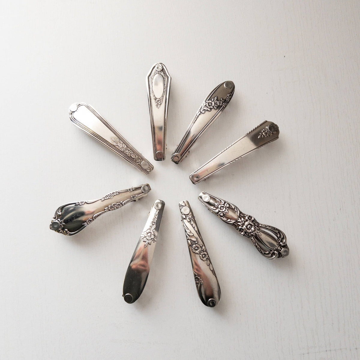 Eight vintage silver-toned ornate hair clips arranged in a circular pattern on a white background.