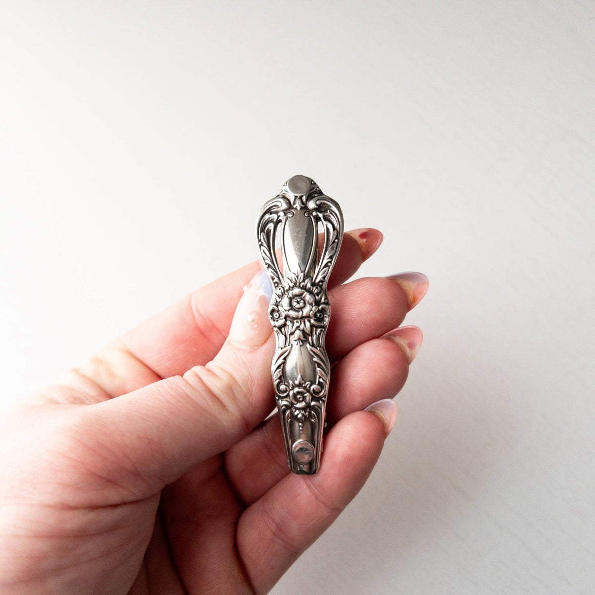 A hand holding a vintage-style ornate silver decorative charm with floral engravings.