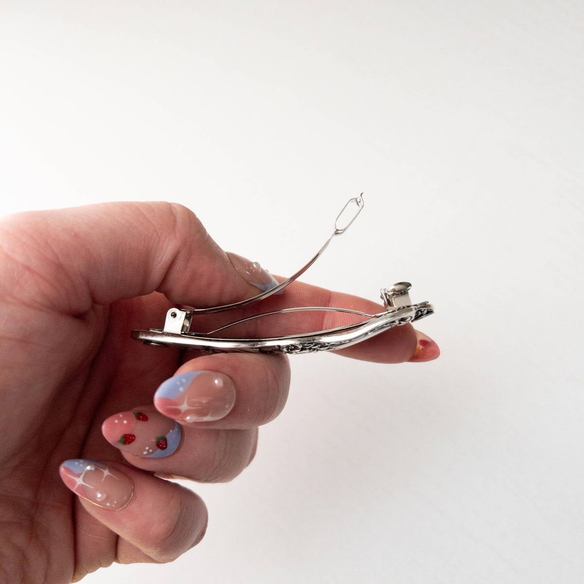 Close-up of a hand holding a silver ornate metal hair clip with detailed engraving.